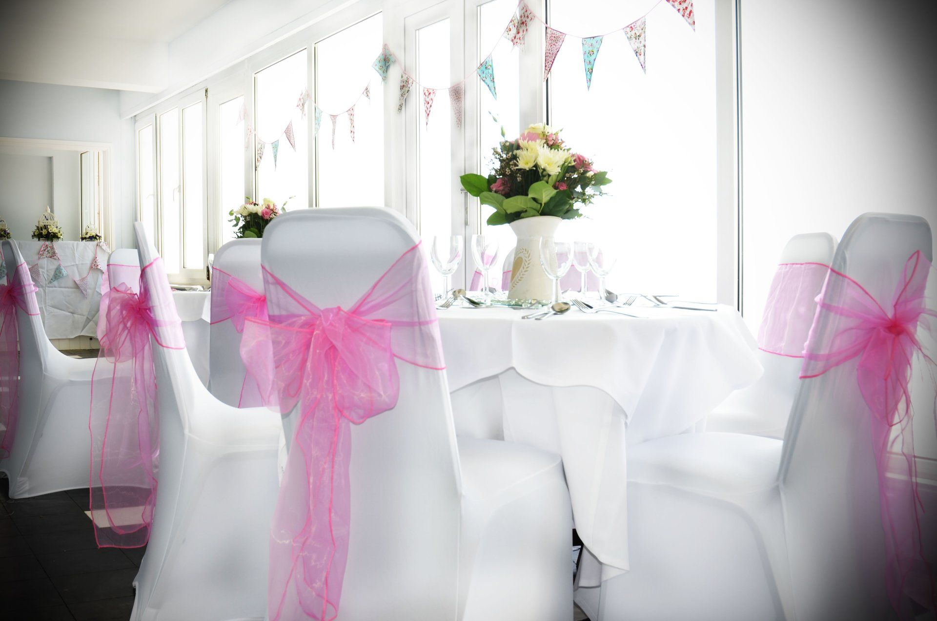 A room with tables and chairs decorated with pink bows.