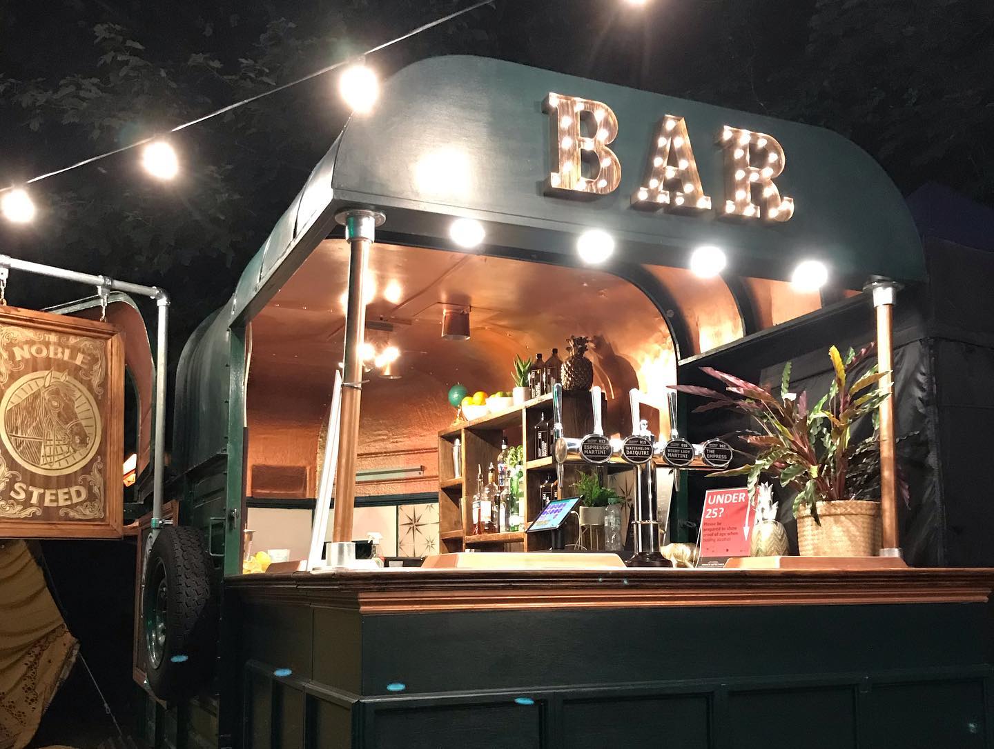 A green bar with a sign that says bar is lit up at night.