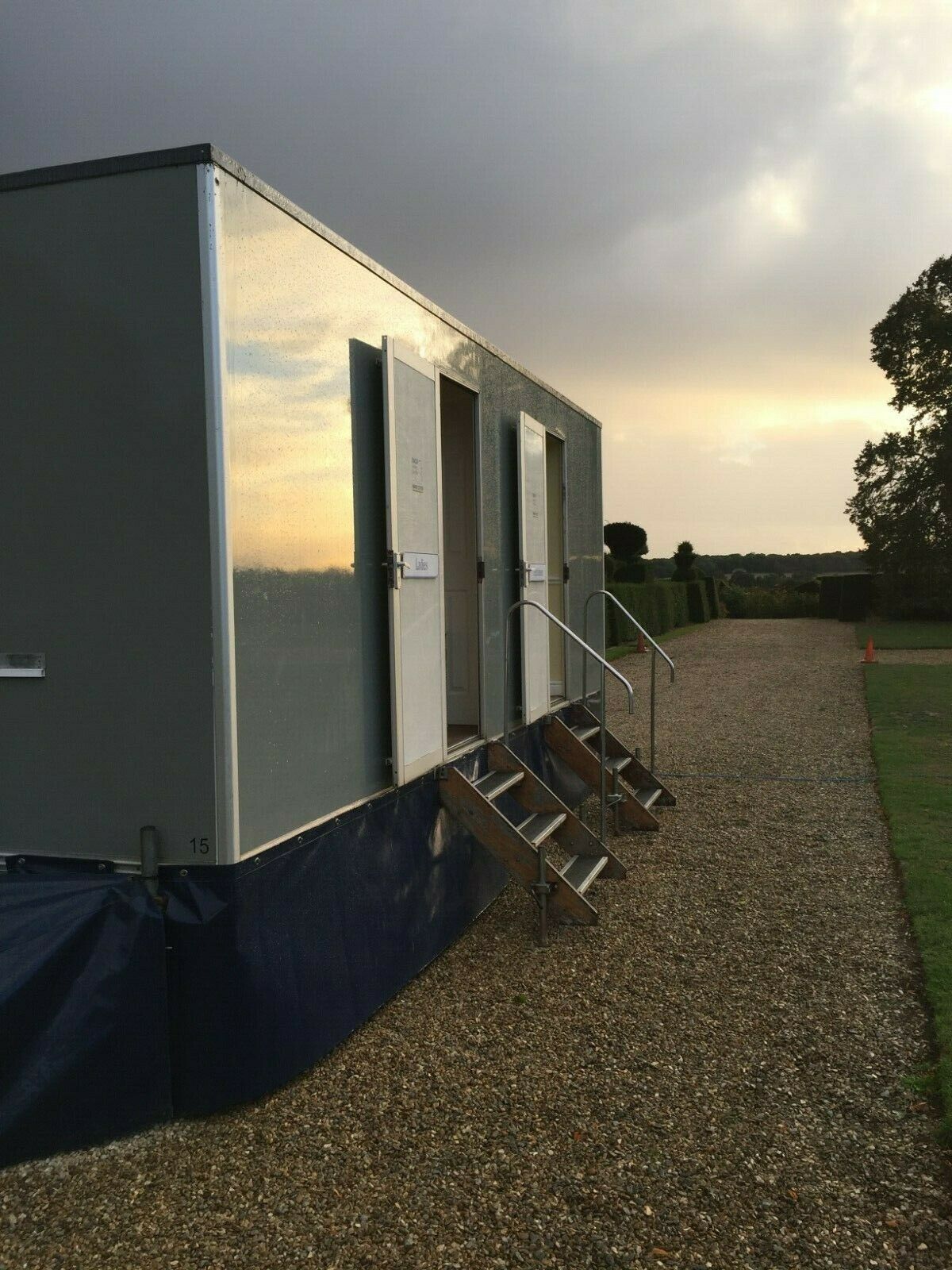 A trailer with stairs leading up to it is parked on a gravel road.