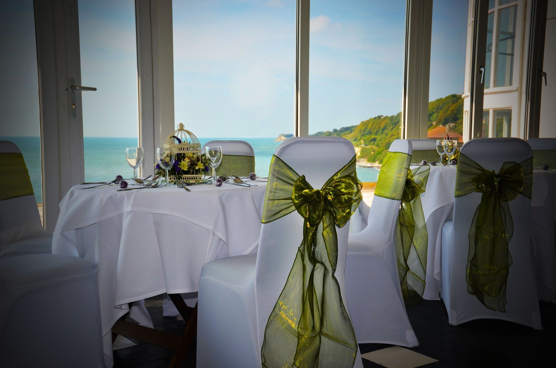A room with tables and chairs decorated for a wedding with a view of the ocean