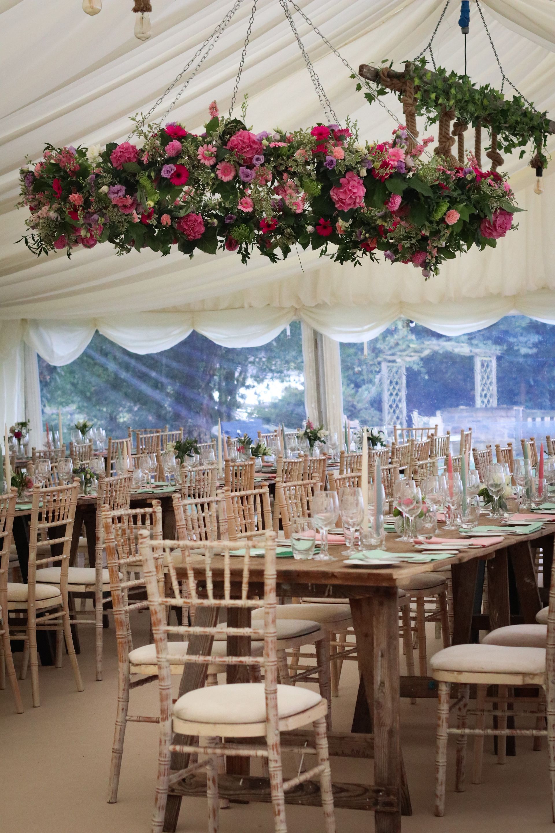 A tent with tables and chairs and flowers hanging from the ceiling