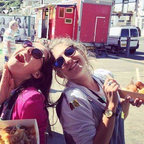 Two women wearing sunglasses are standing next to each other in front of a food truck.