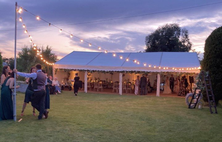 A group of people are dancing under a tent at a wedding reception.