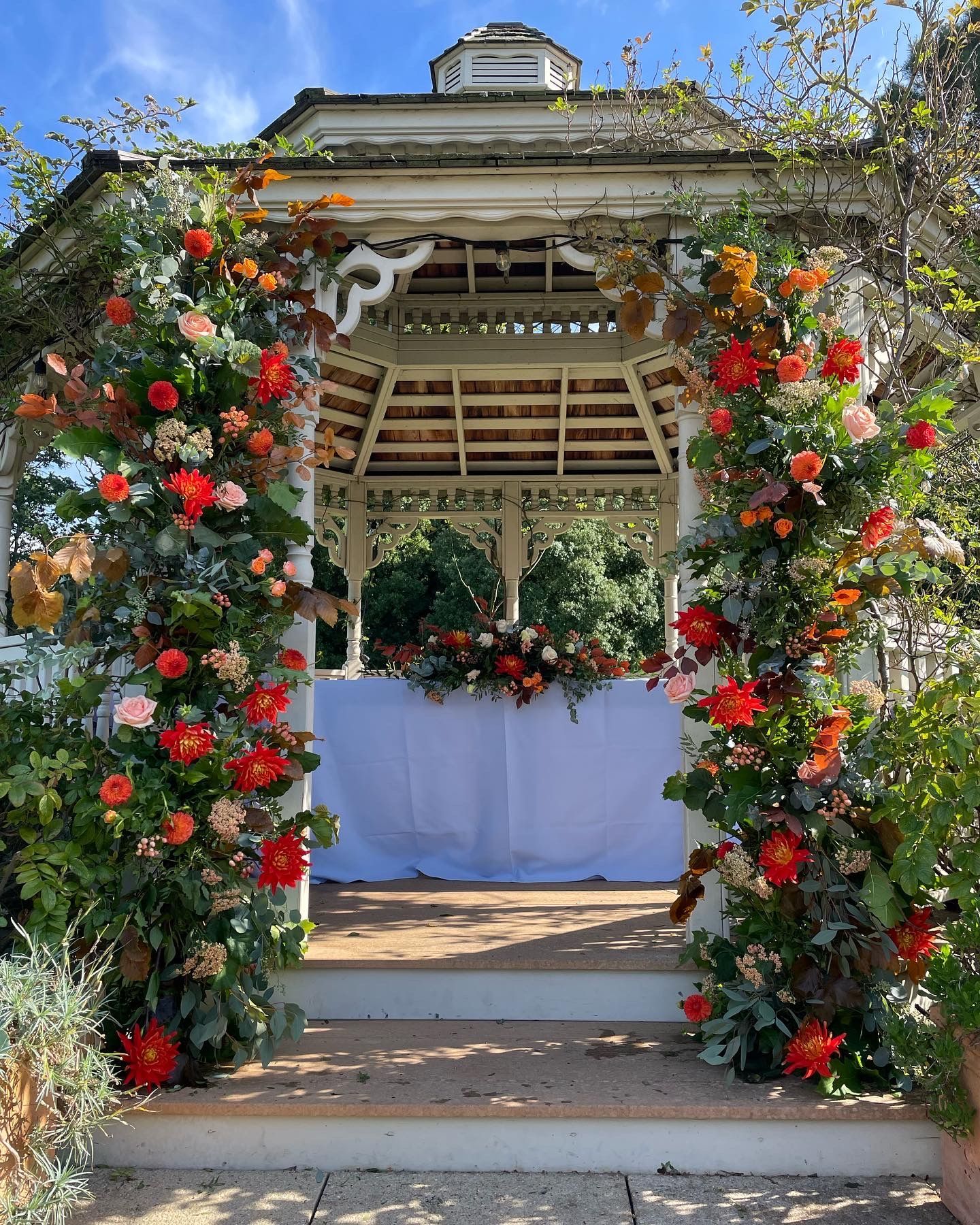A gazebo is decorated with flowers and leaves for a wedding ceremony.