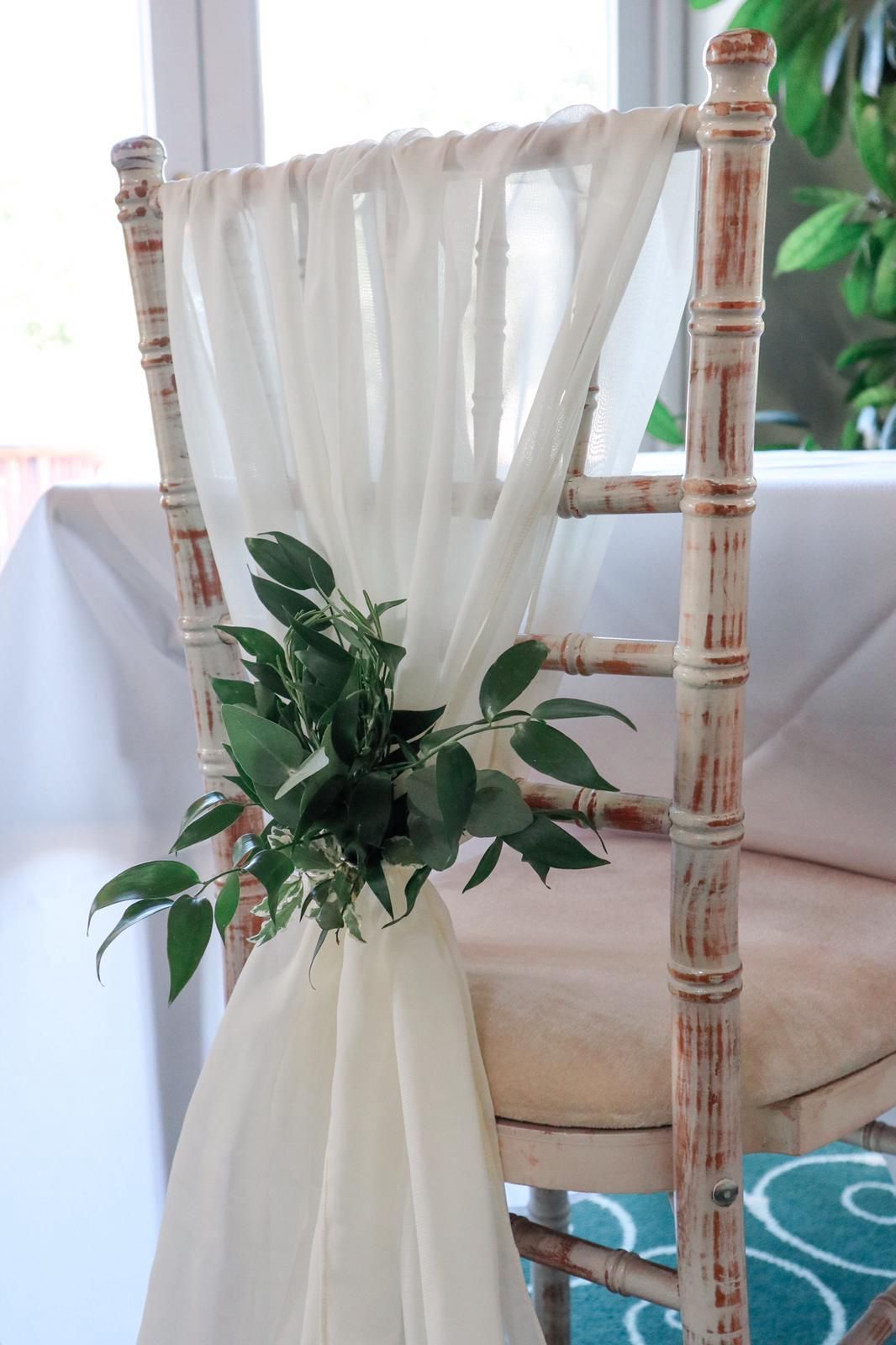 A chair with a white curtain and green leaves on it.
