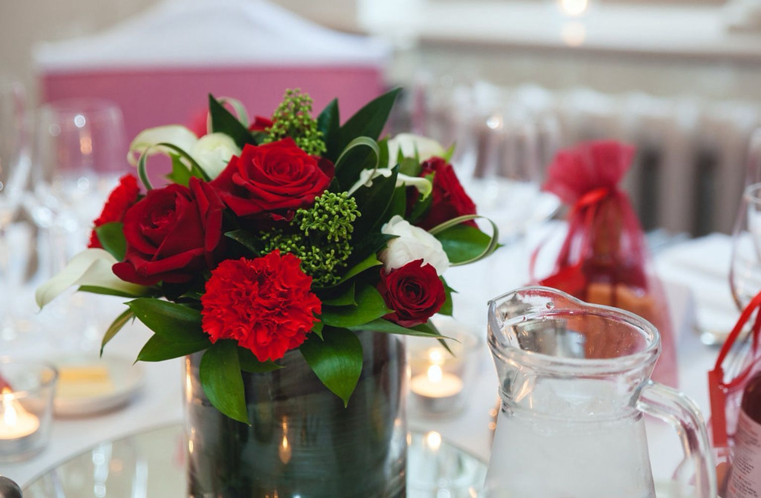 A vase filled with red roses and carnations sits on a table.