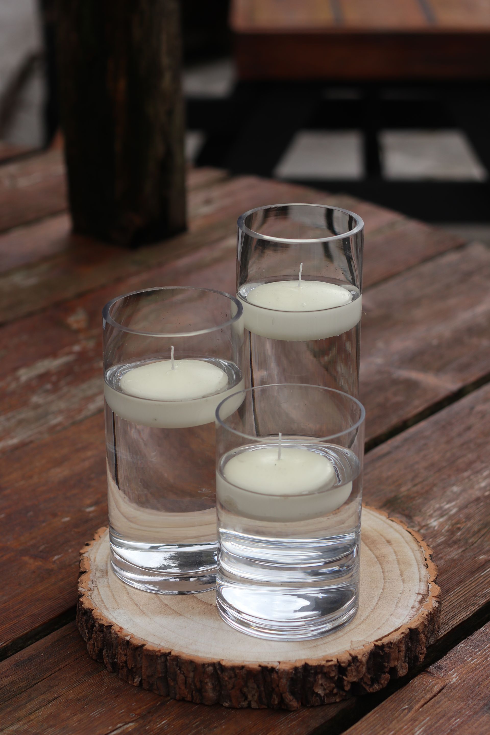 Three glasses of water with candles in them on a wooden table.