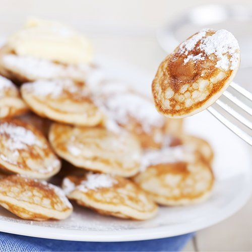 A close up of a fork holding a pancake over a plate of pancakes