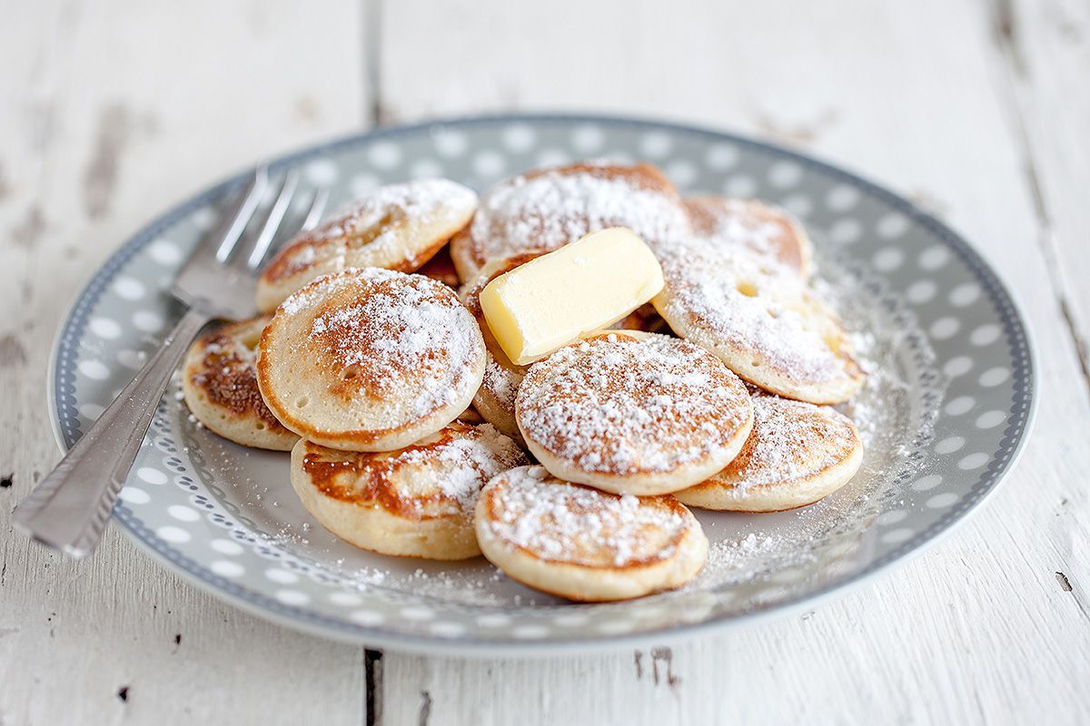A plate of pancakes with butter and powdered sugar on a table.