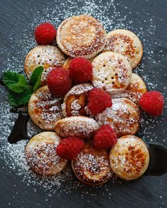 A plate of pancakes with raspberries and powdered sugar on a table.