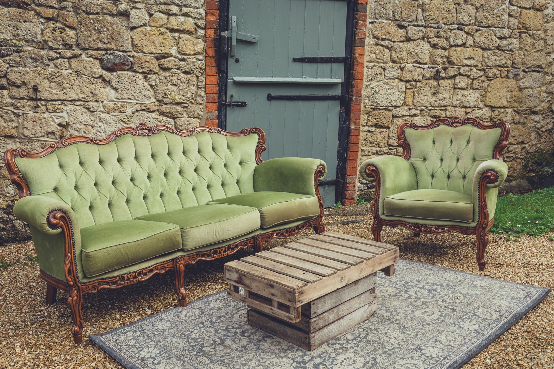 A green couch , chair , and coffee table are sitting in front of a stone wall.