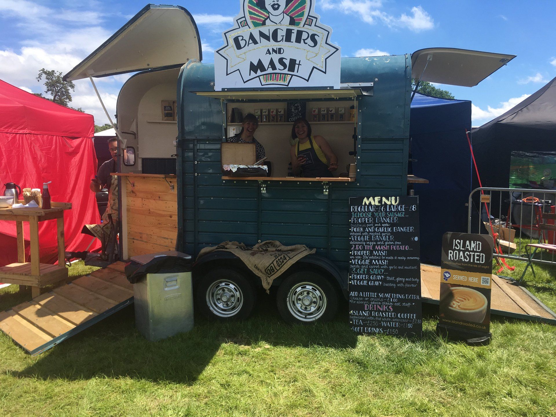 A food truck is parked in the grass in front of a red tent.