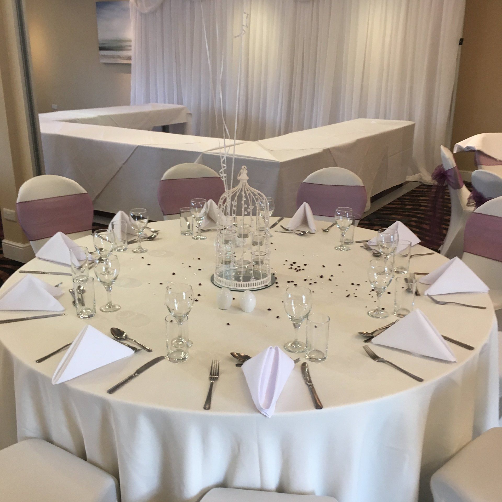 A round table with white linens and purple chairs