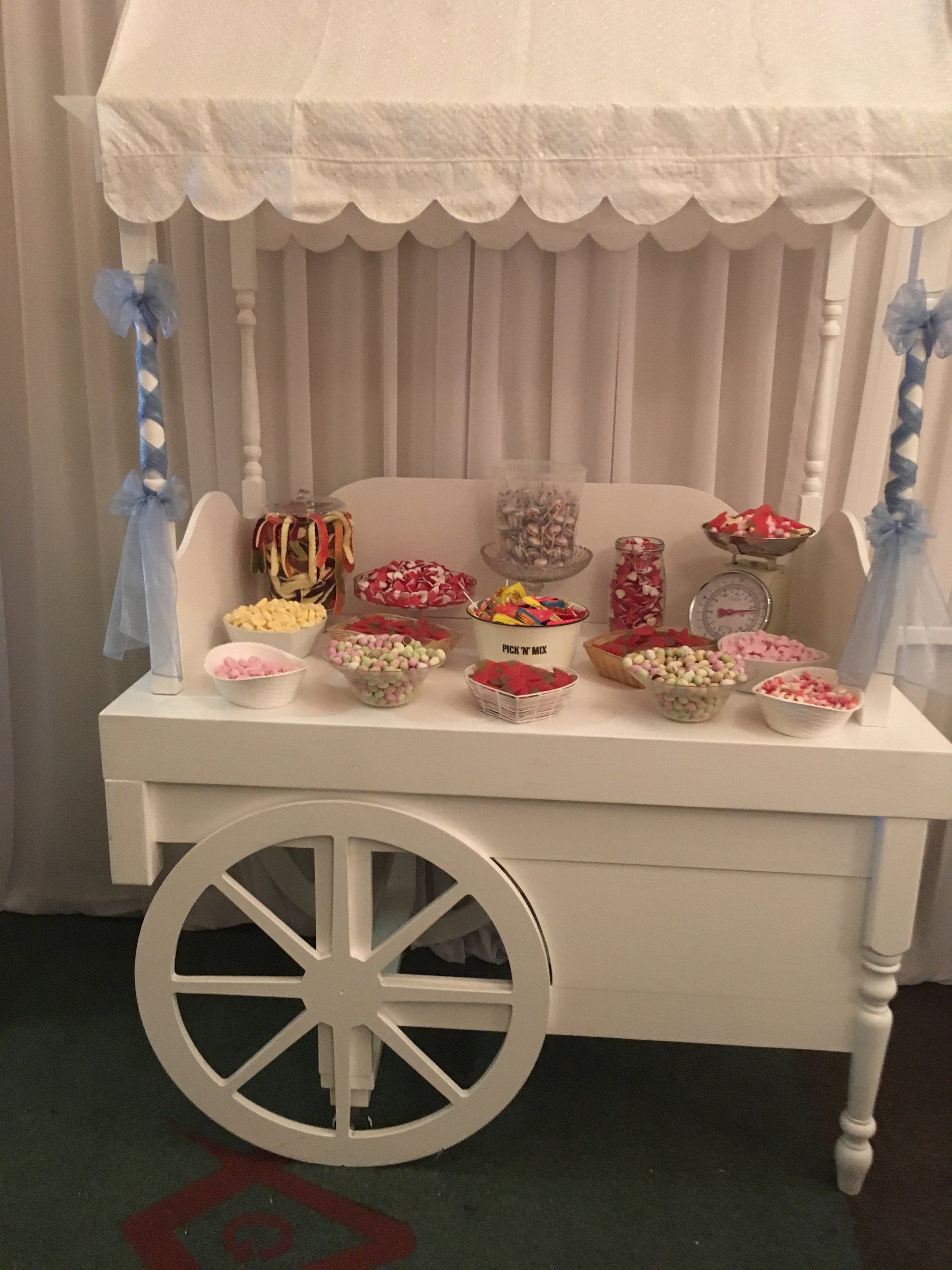 A white candy cart filled with candy and a canopy.