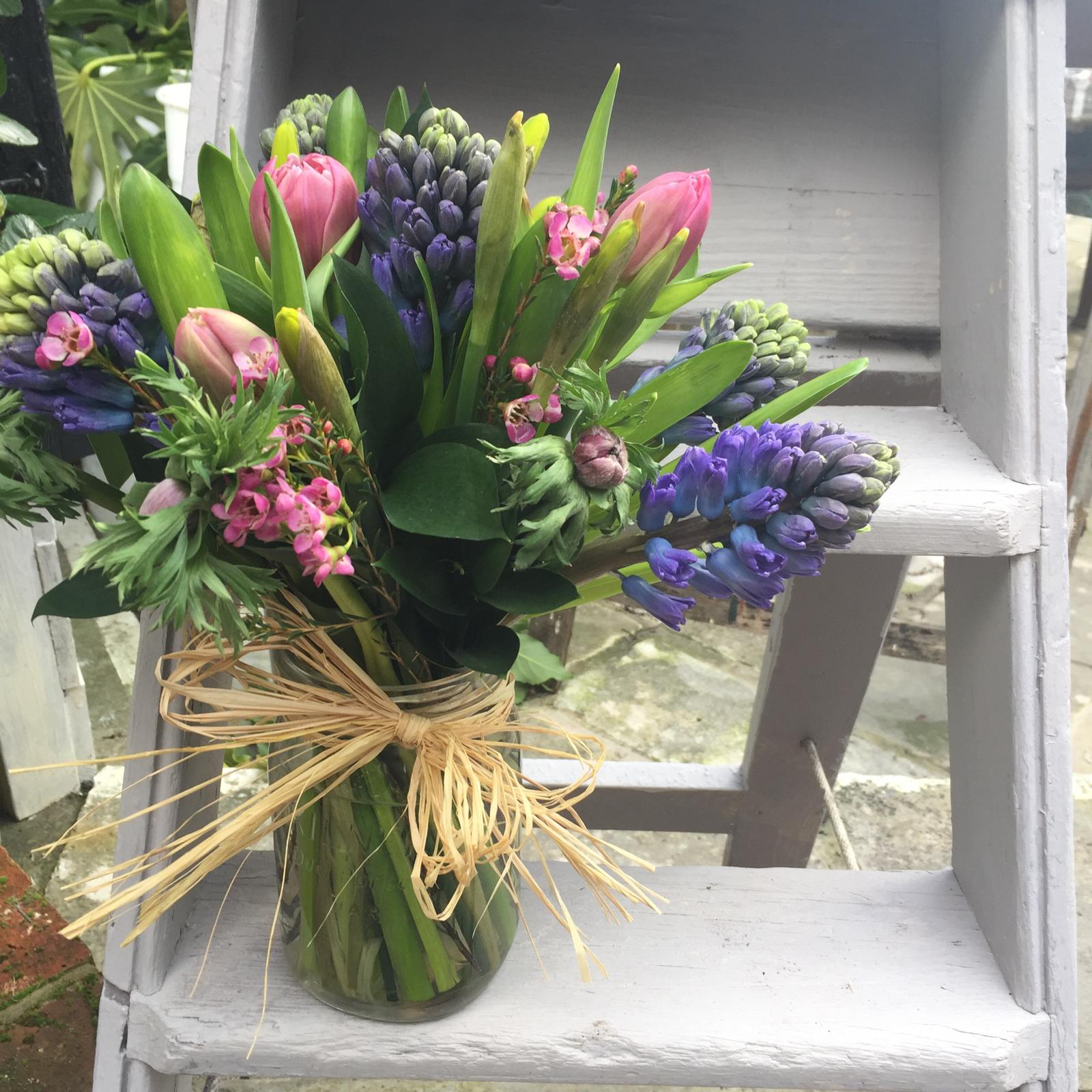 A vase filled with flowers is sitting on a ladder.