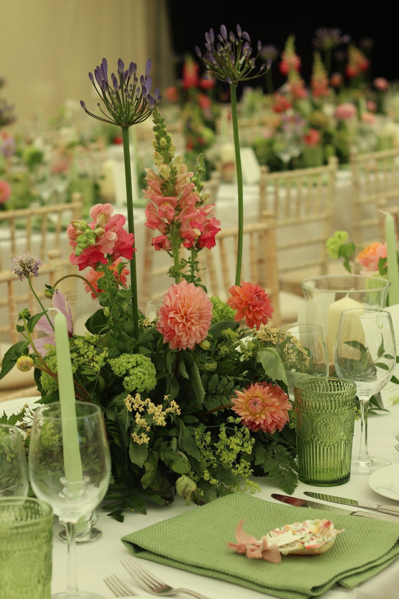 A table set for a wedding reception with flowers , candles , glasses and napkins.