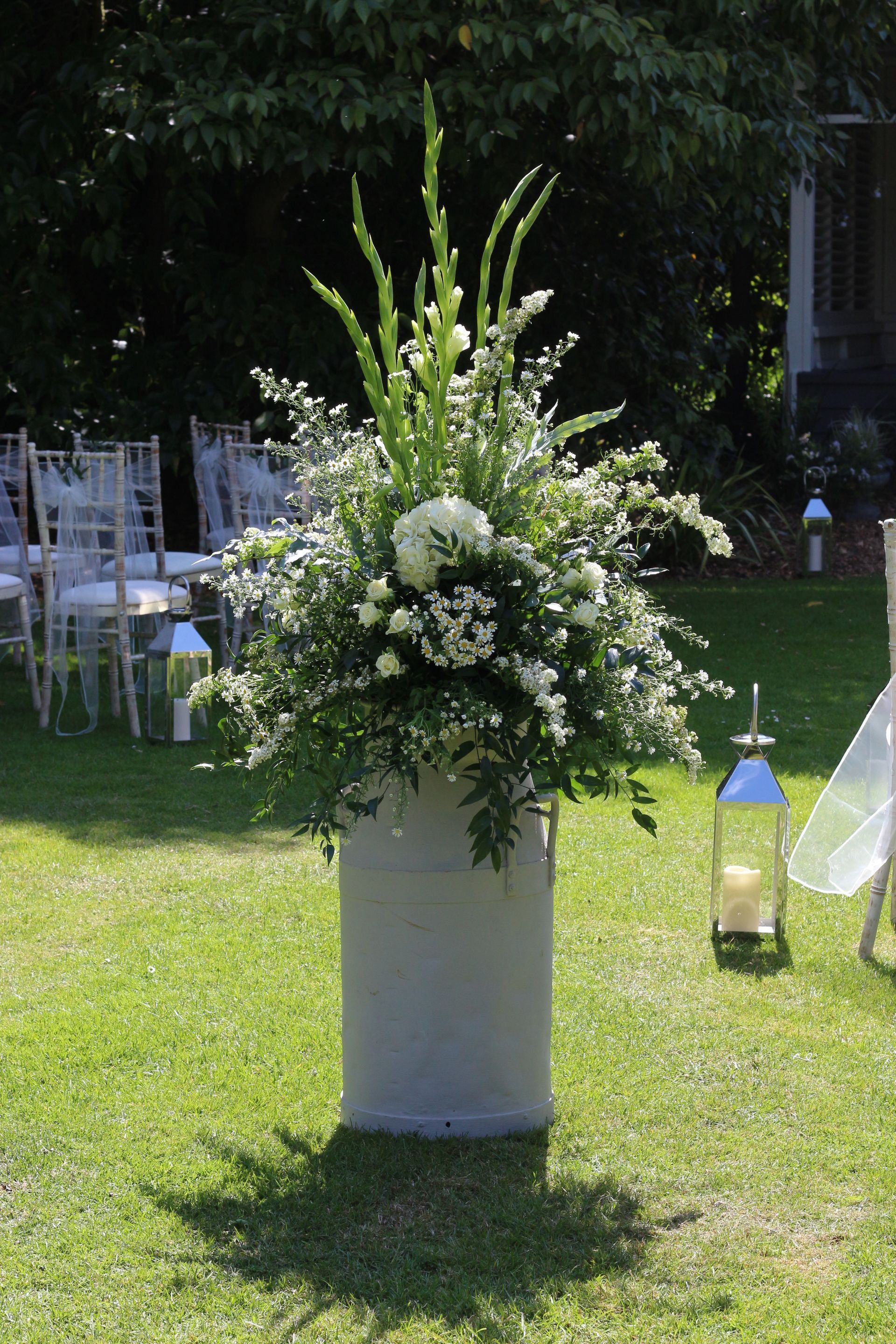 A large vase filled with white flowers is sitting in the grass.