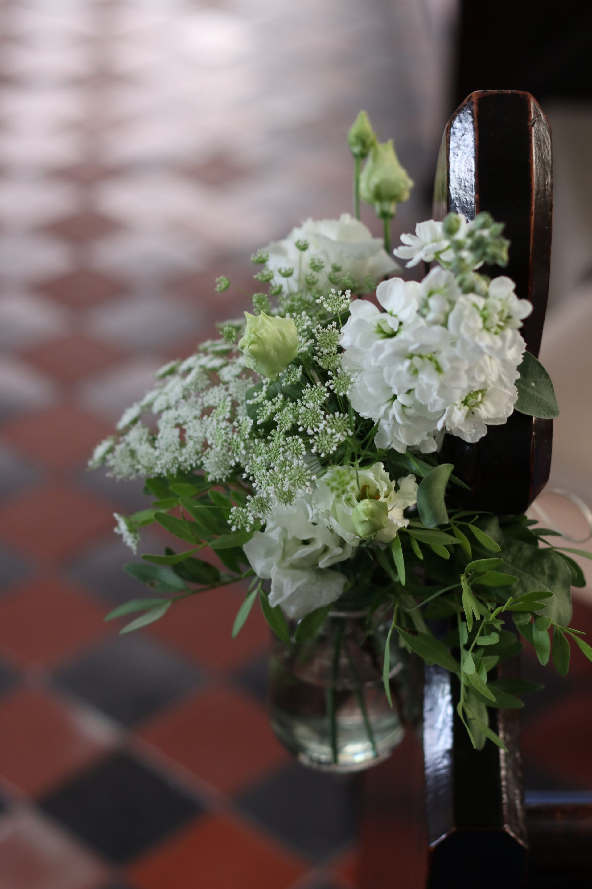 A vase filled with white flowers is sitting on a church bench.