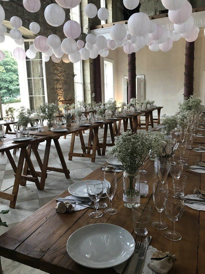 A long wooden table with plates , glasses , and vases on it.