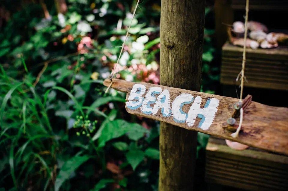 A wooden sign that says beach is hanging from a tree.