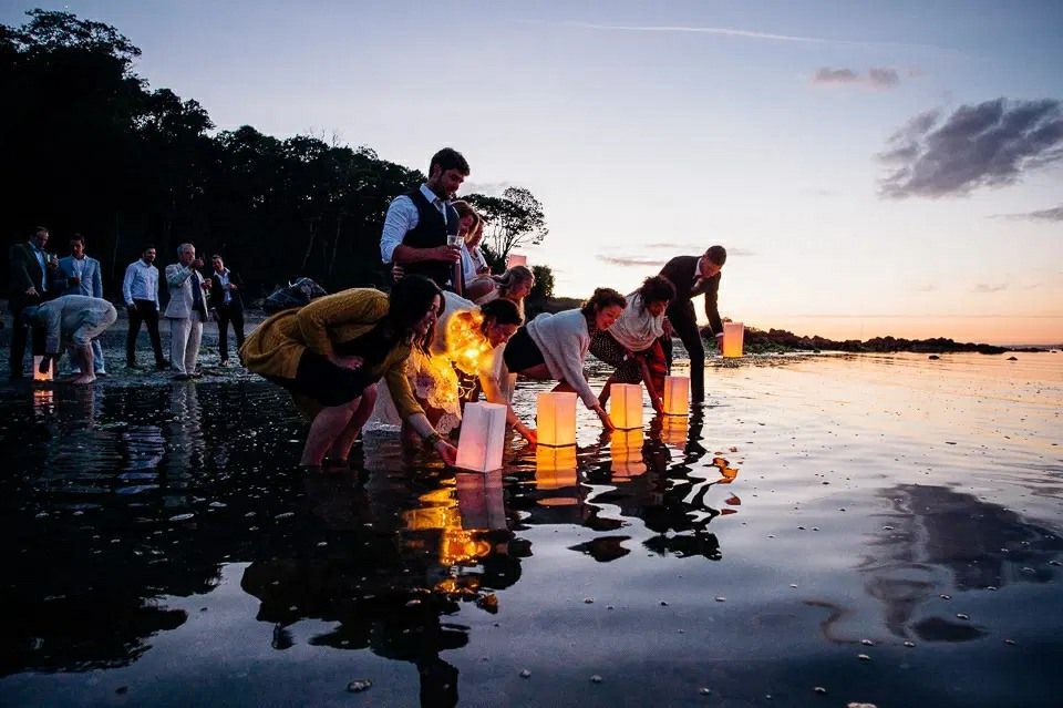 A group of people are kneeling in the water holding lanterns.