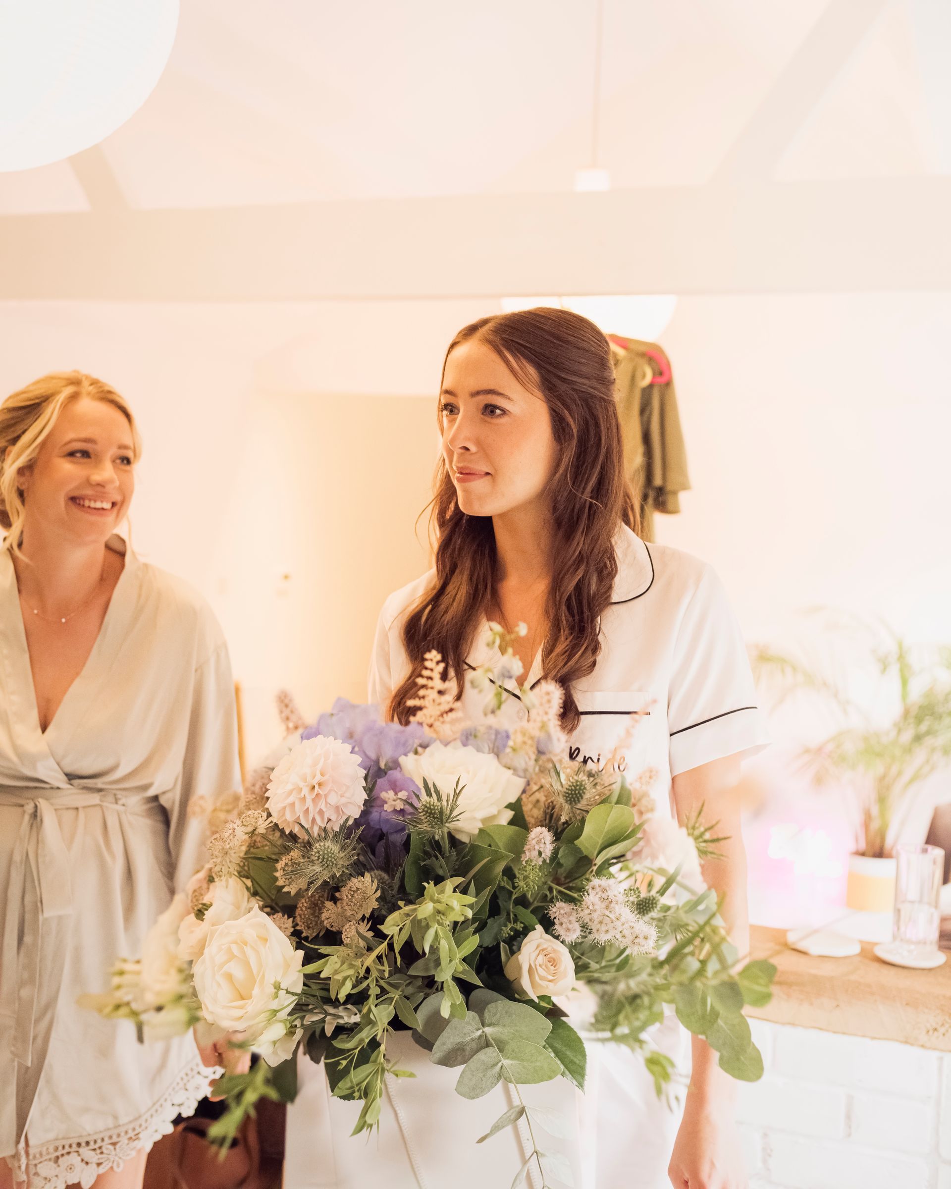 Two women are standing next to each other in a room holding a bouquet of flowers.