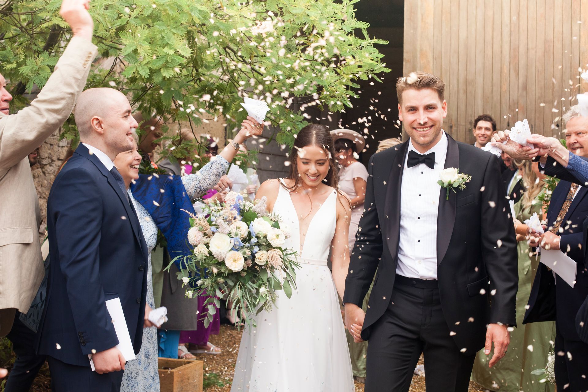 A bride and groom are walking through a crowd of people throwing confetti at them.