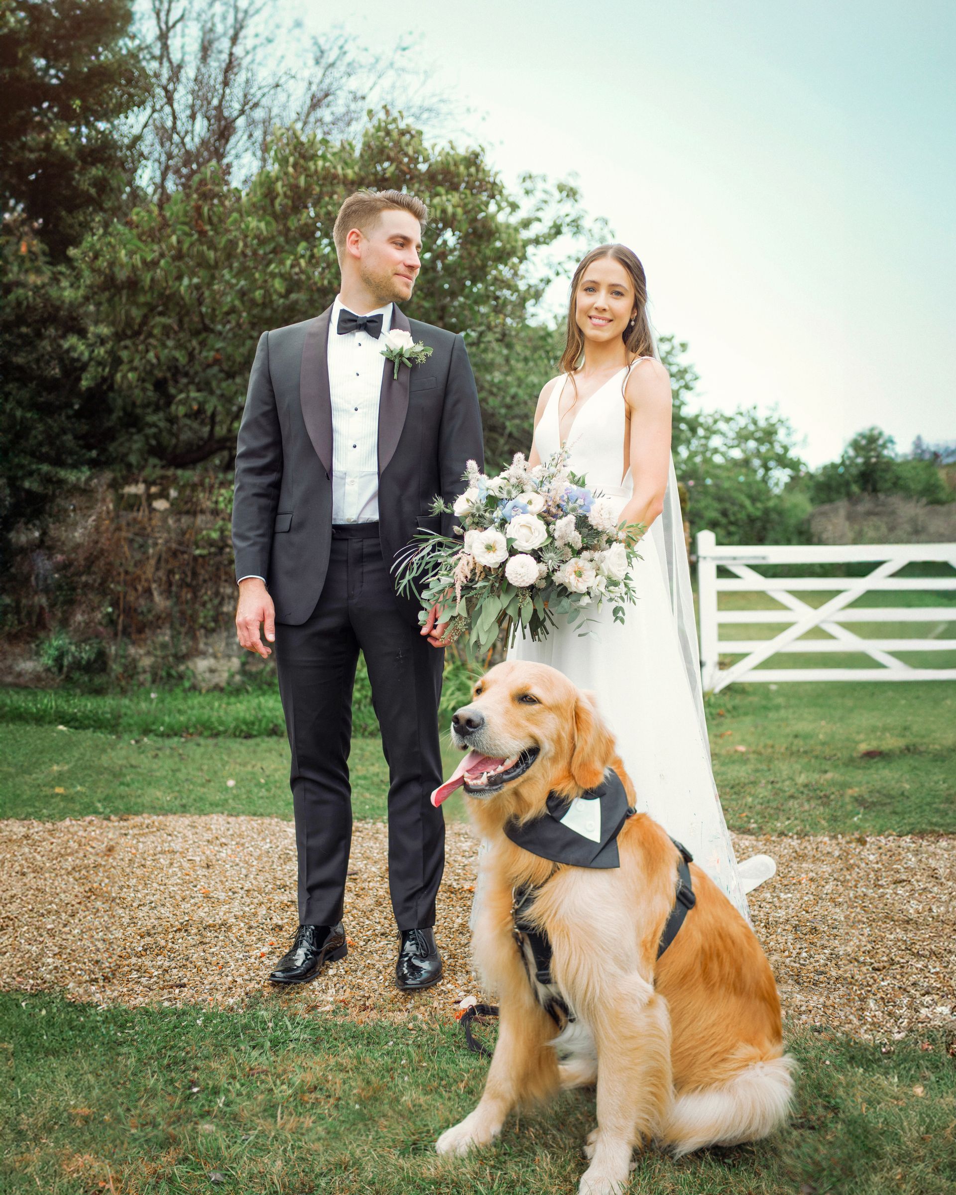 A bride and groom are posing for a picture with their dog.