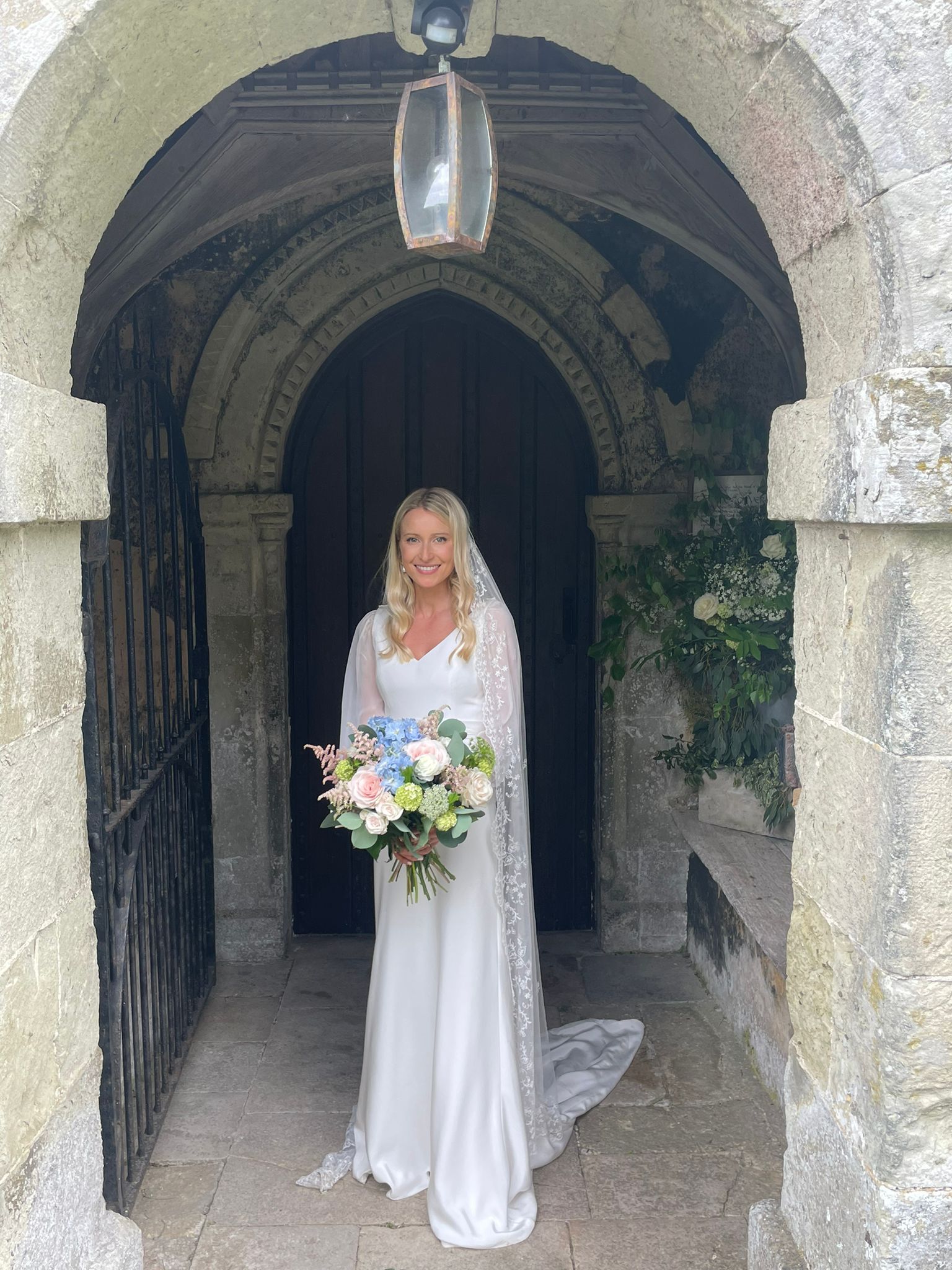 A woman in a wedding dress is standing in front of a door holding a bouquet of flowers.
