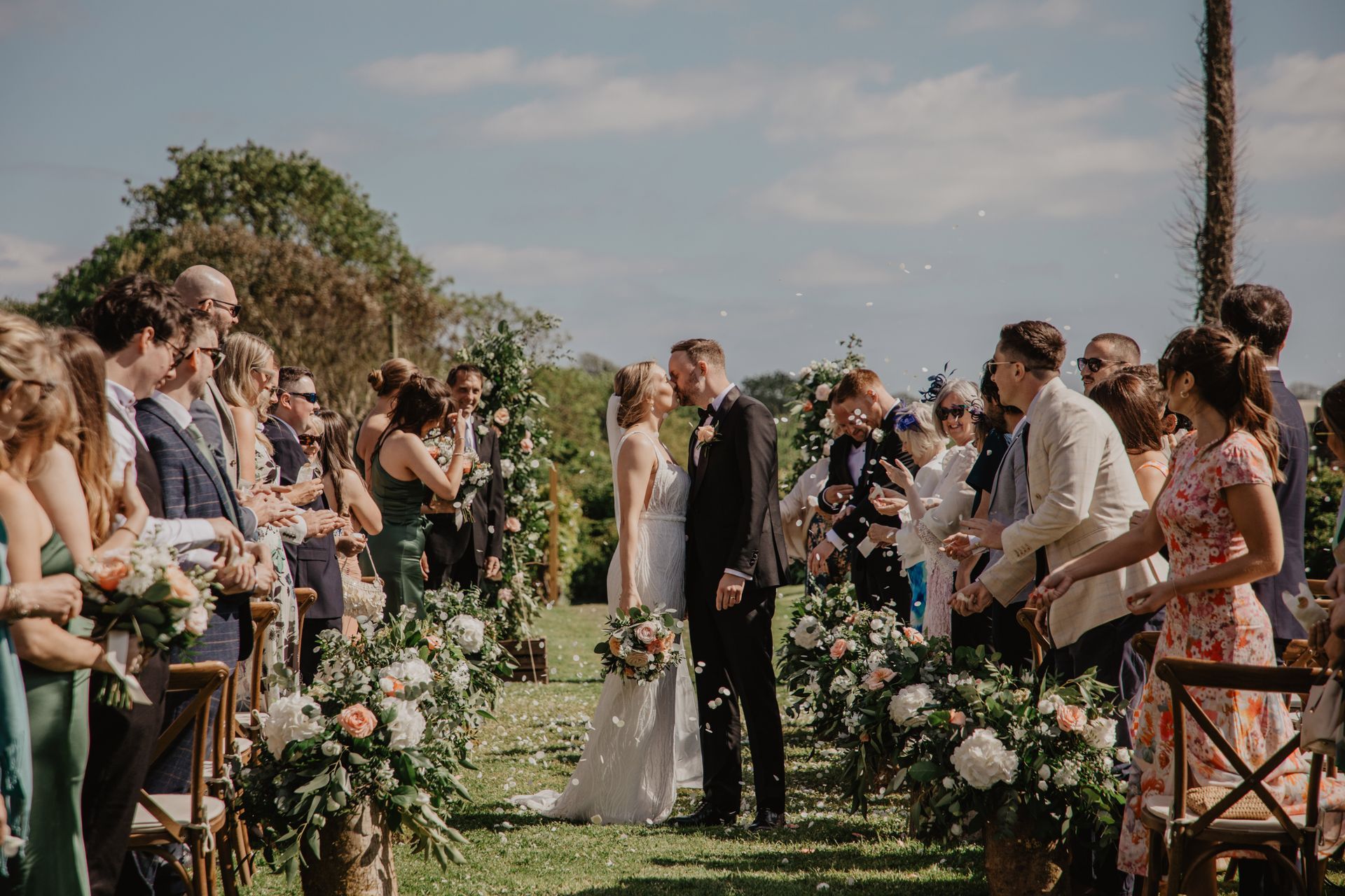 A bride and groom are kissing during their wedding ceremony while their wedding guests watch.