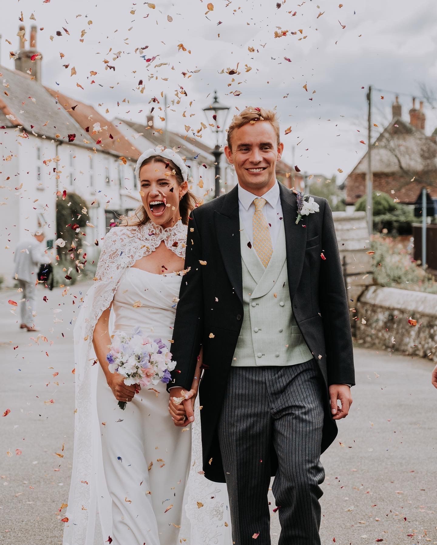 A bride and groom are walking down a street with confetti falling around them.