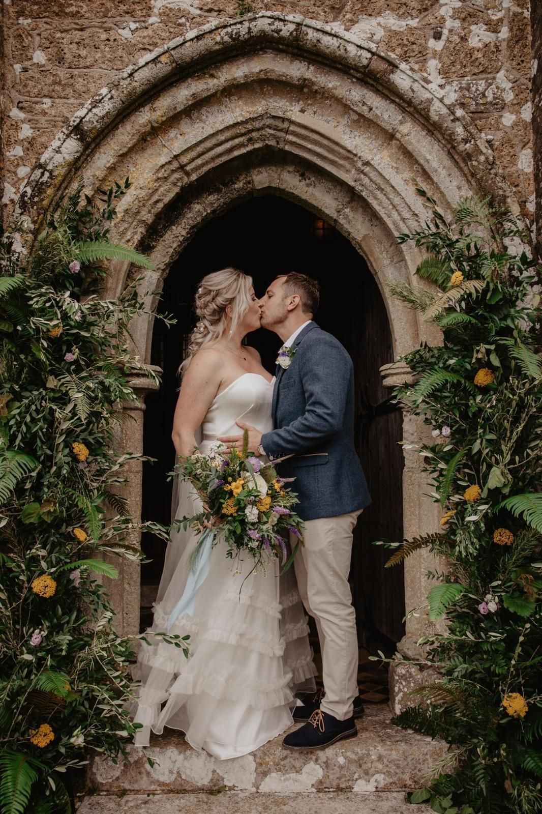 A bride and groom are kissing in front of a stone archway.