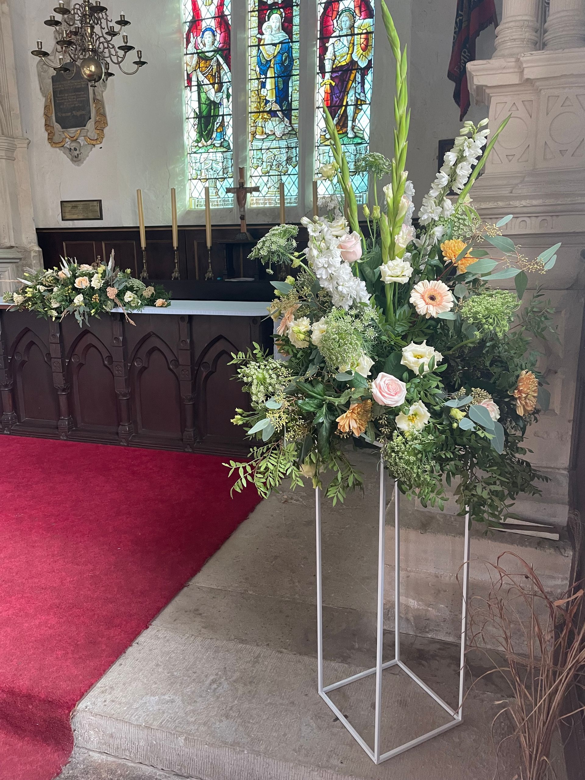 A church with flowers on a stand in front of a stained glass window.