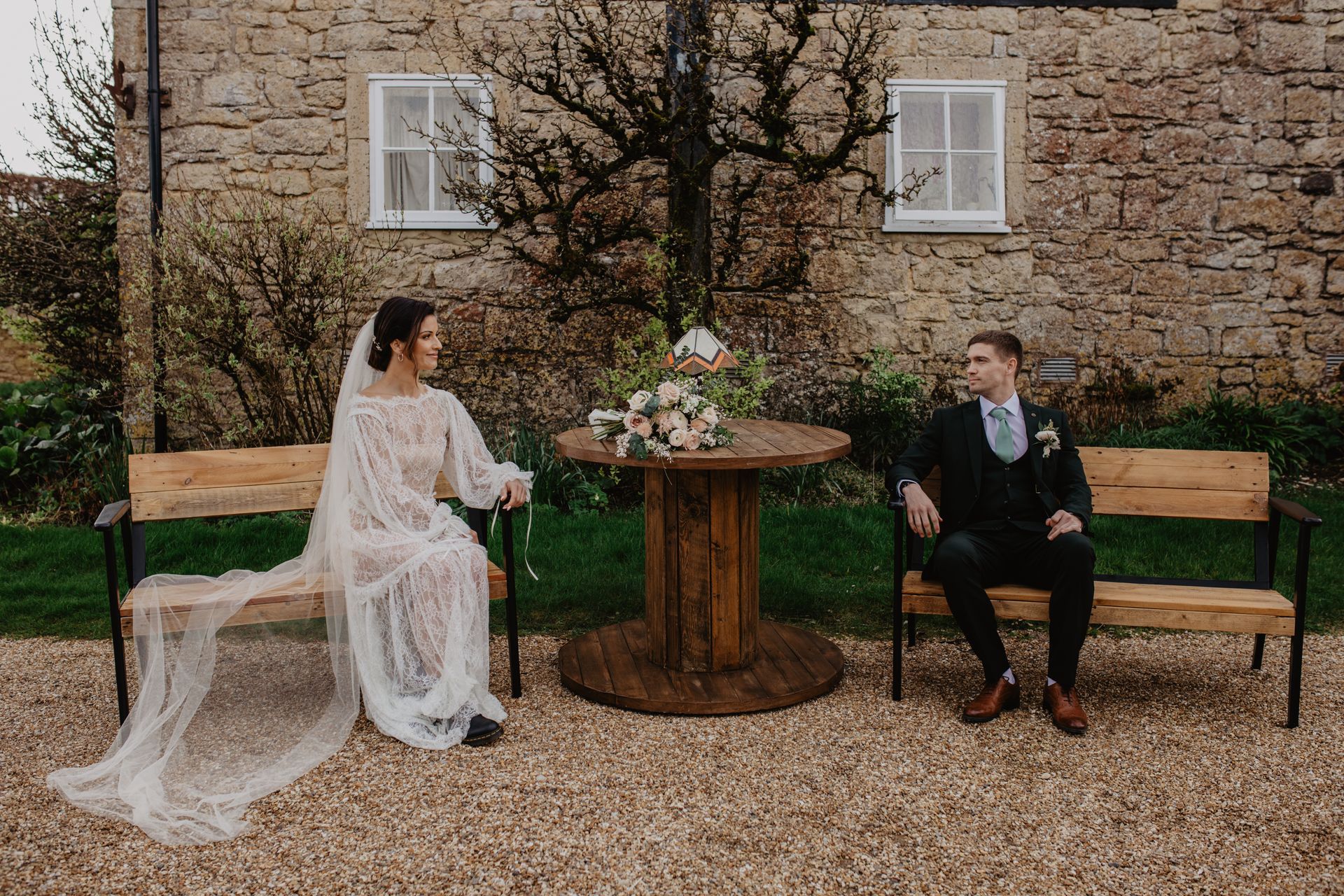 A bride and groom are sitting on a bench in front of a stone building.