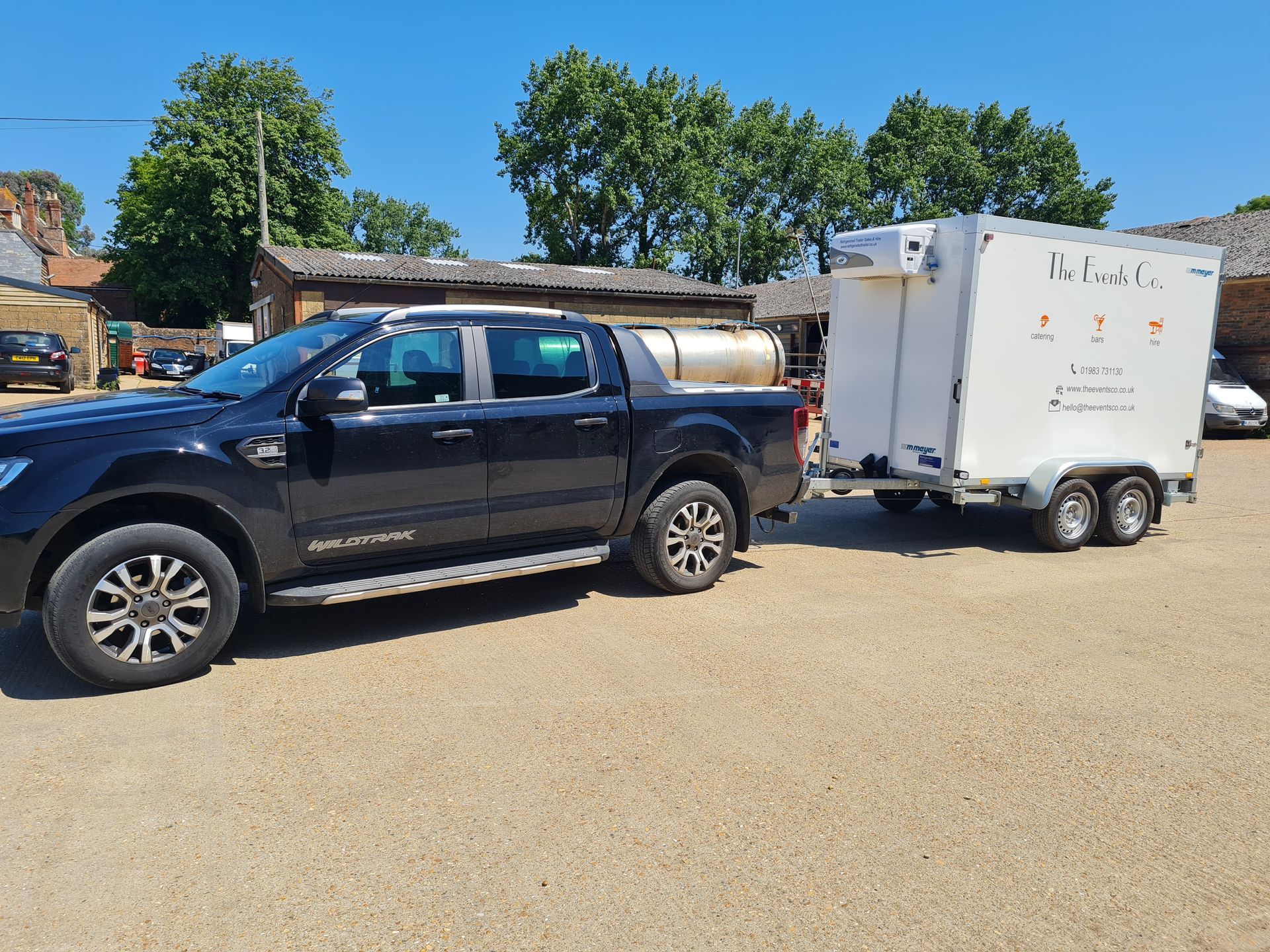 A black truck is towing a white trailer in a parking lot.