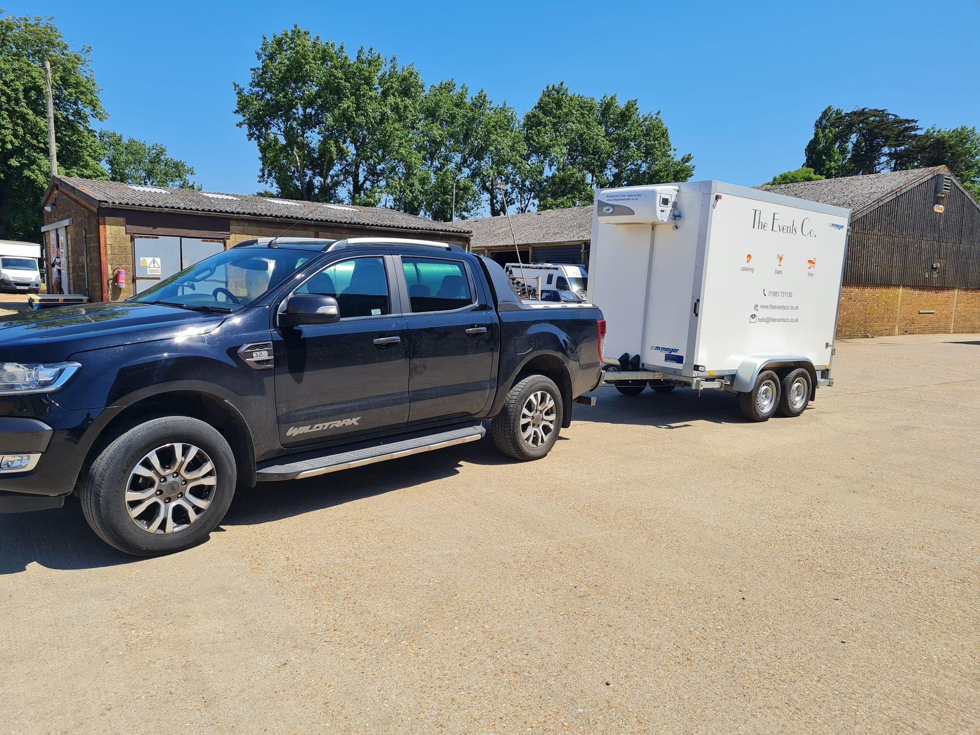 A black truck is towing a white trailer in a parking lot.