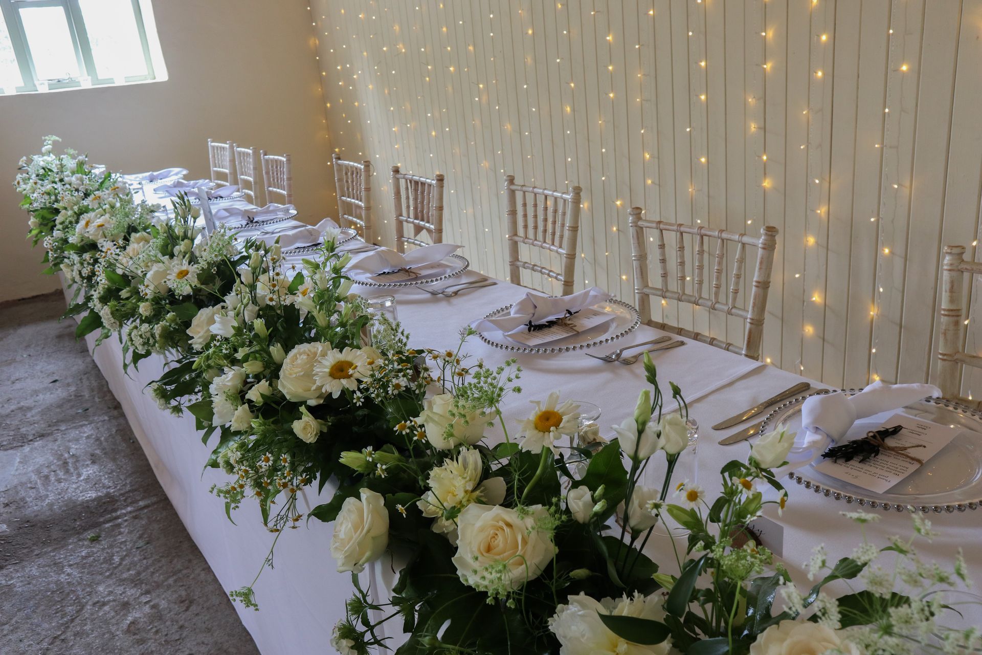 A long table with plates , utensils , and flowers on it.