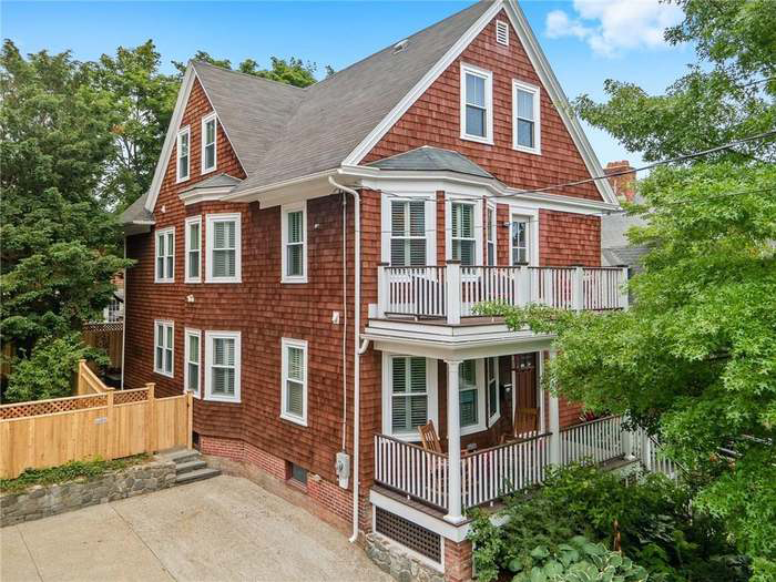 An aerial view of a large red brick house with a white porch surrounded by trees.