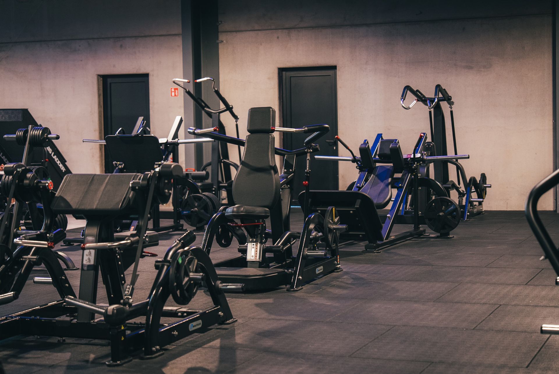 Interieur van de sportschool met verschillende gewichtsapparaten, zwarte rubberen vloer en neutrale muren.