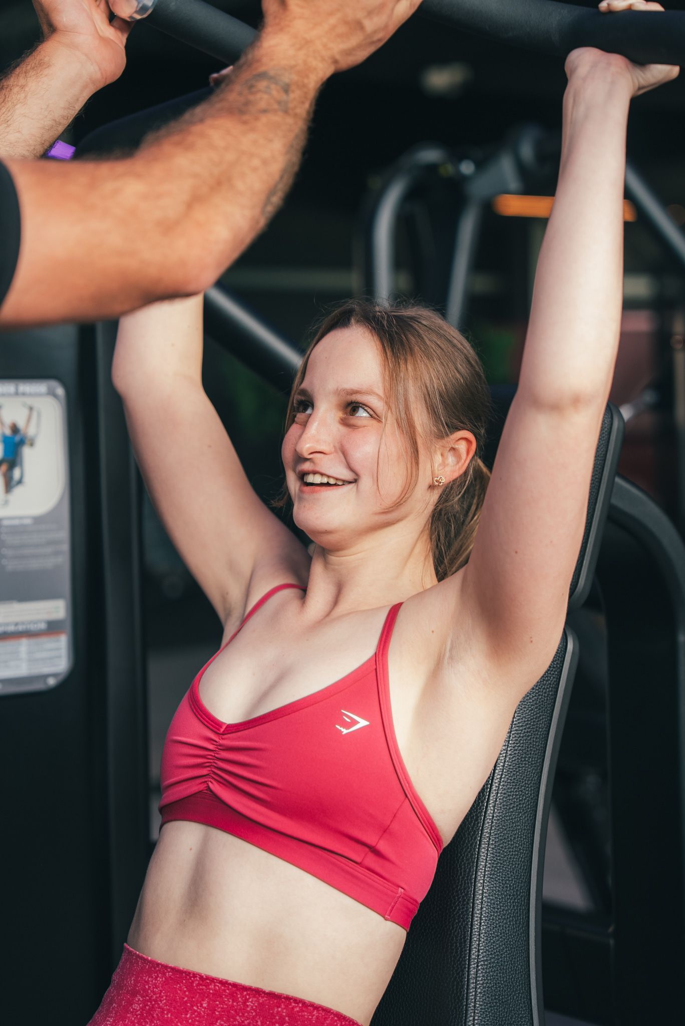 Vrouw doet een borstpersoefening met een trainer in een buitensportschool. Rode sportkleding.