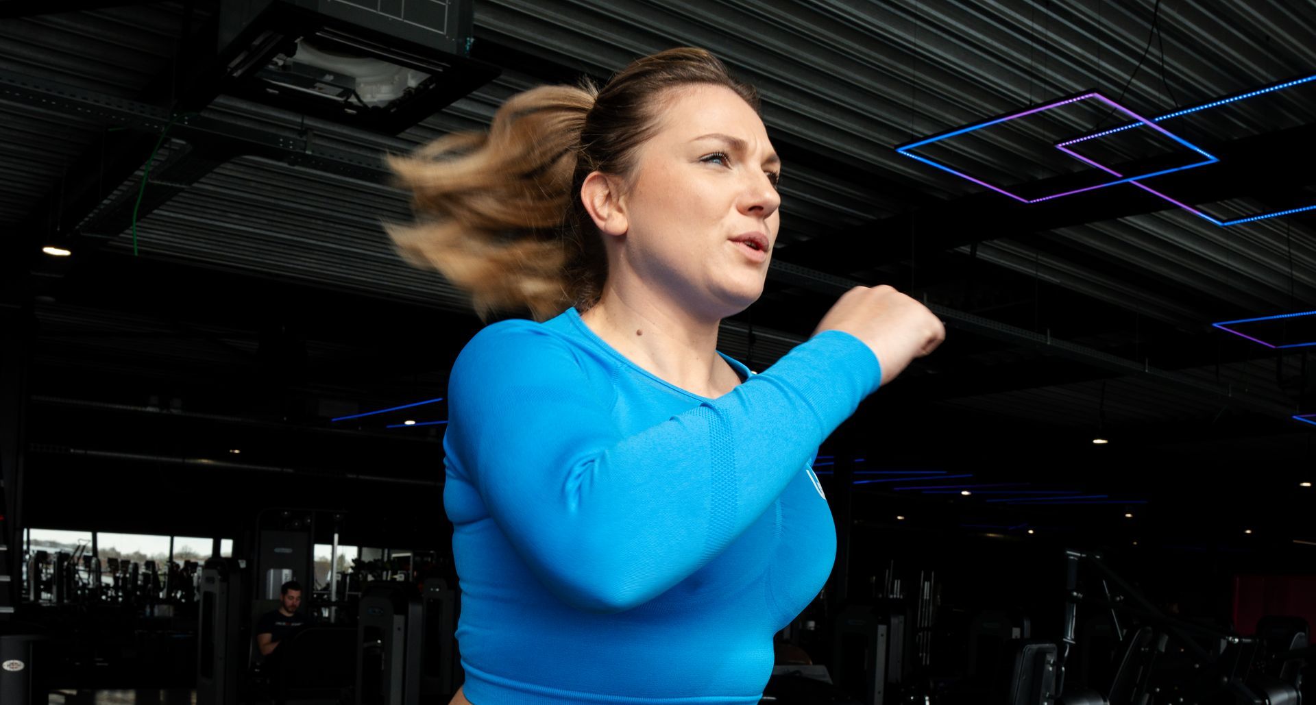 Een vrouw in een blauw shirt rent in een sportschool.