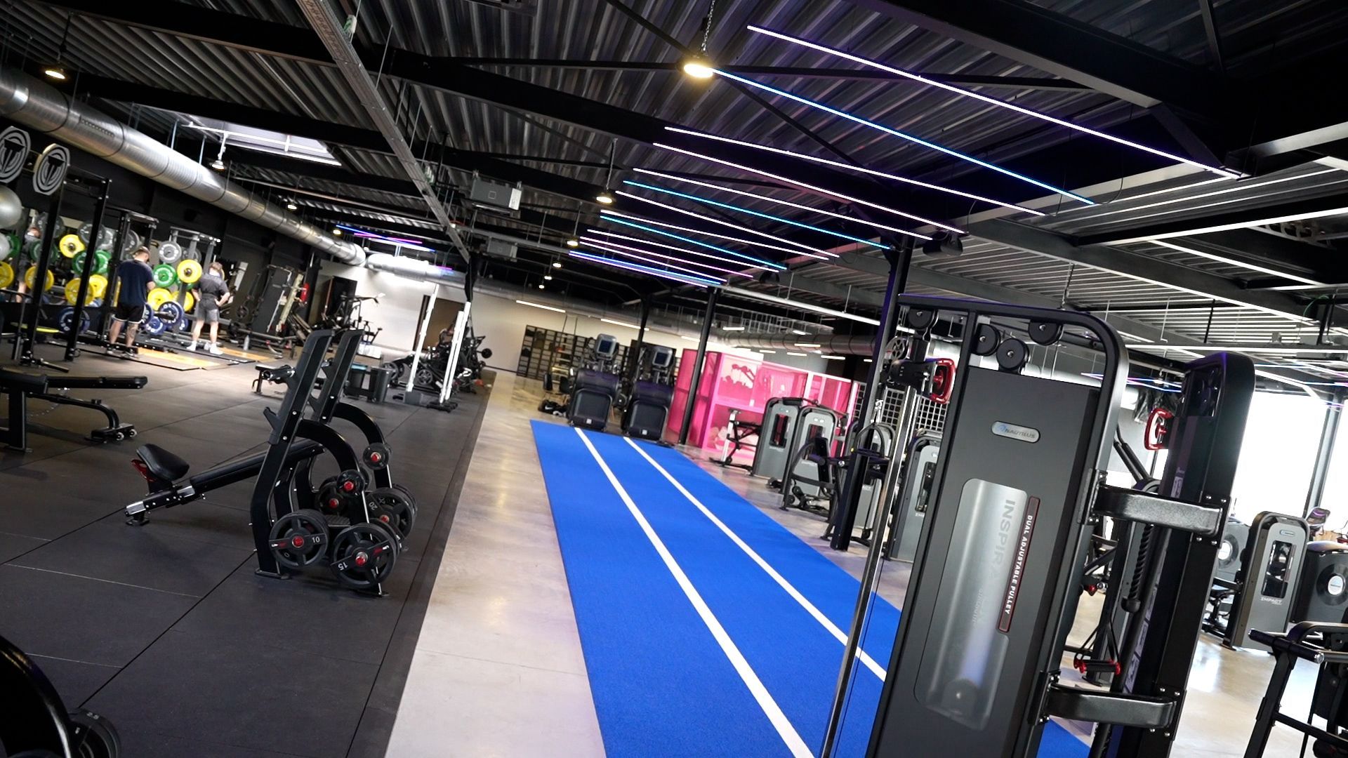 Een sportschool vol met fitnessapparatuur en een blauwe mat.