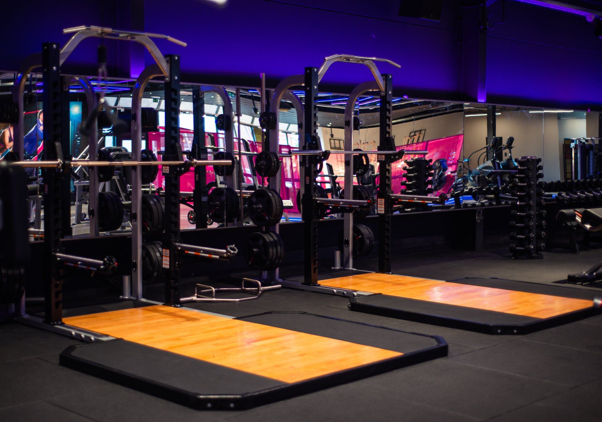 Een sportschool met veel fitnessapparatuur en een houten vloer.
