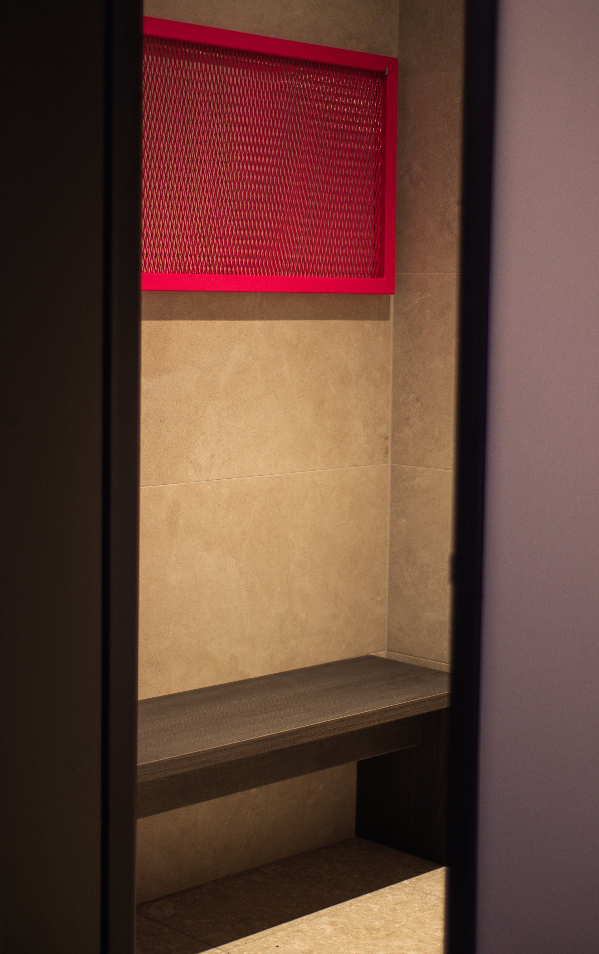 Een kast met een bankje en een rood frame aan de muur.