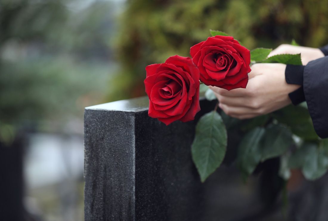 Una mano che posa dei fiori su una lapide funebre