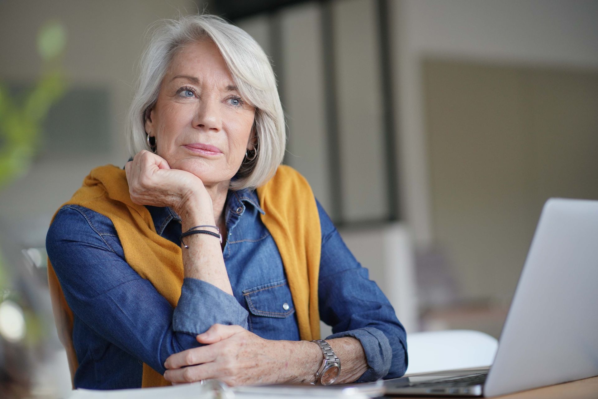 Woman in a light-colored vest smiles while sitting on a couch. Interview setting, with a notepad in focus.