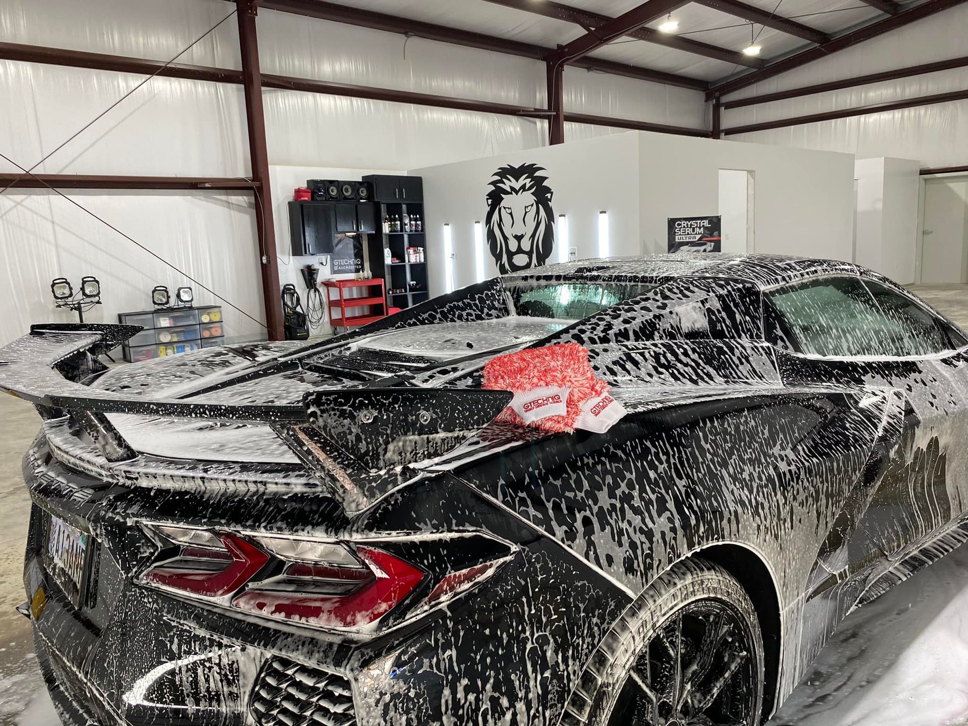 A black sports car is covered in foam in a garage.