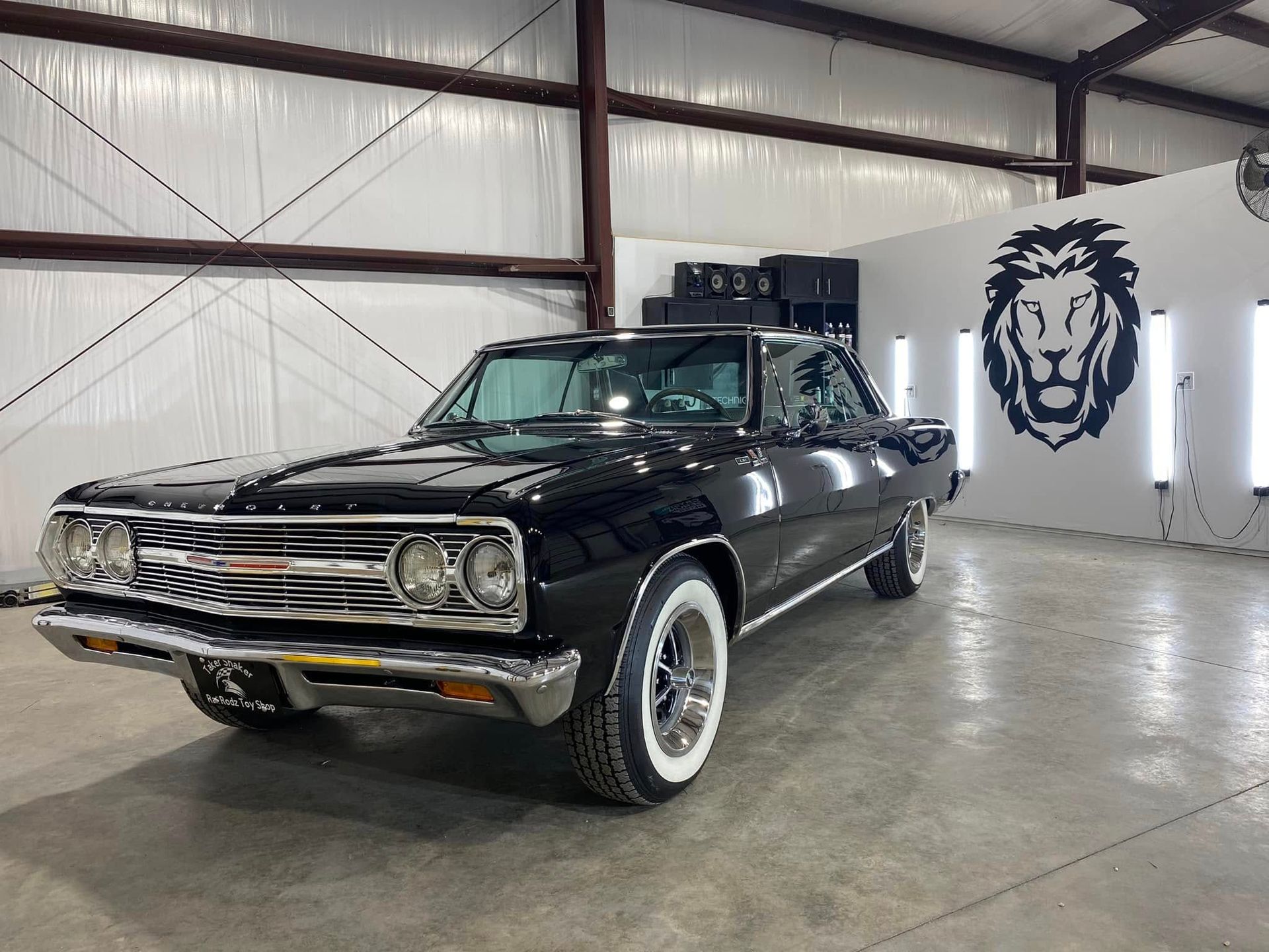 A black car is parked in a garage with a lion on the wall.