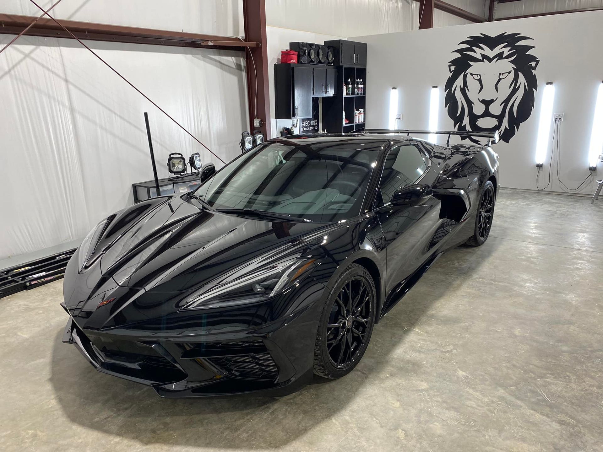 A black sports car is parked in a garage with a lion on the wall.
