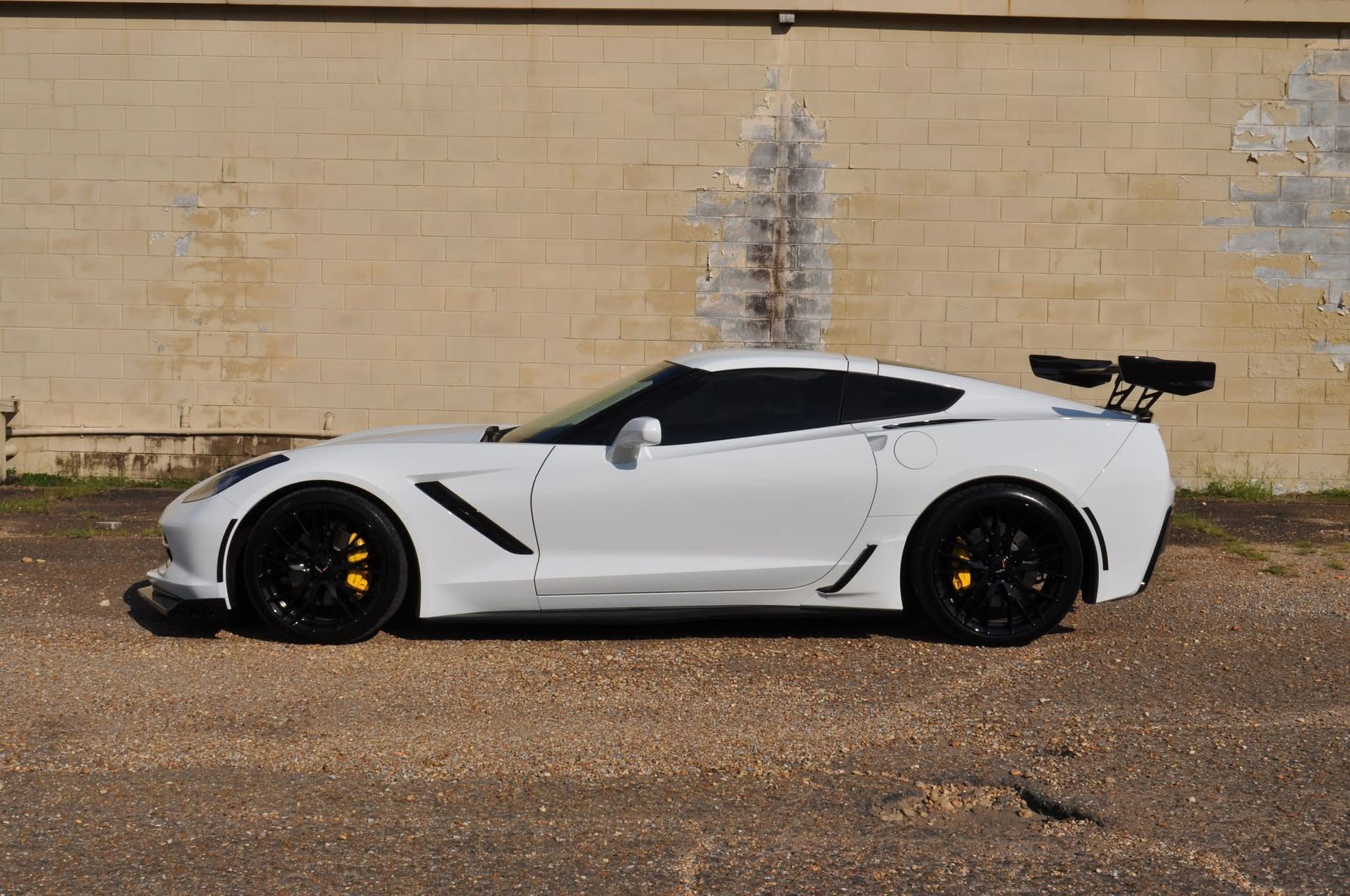 A white sports car is parked in front of a brick wall.
